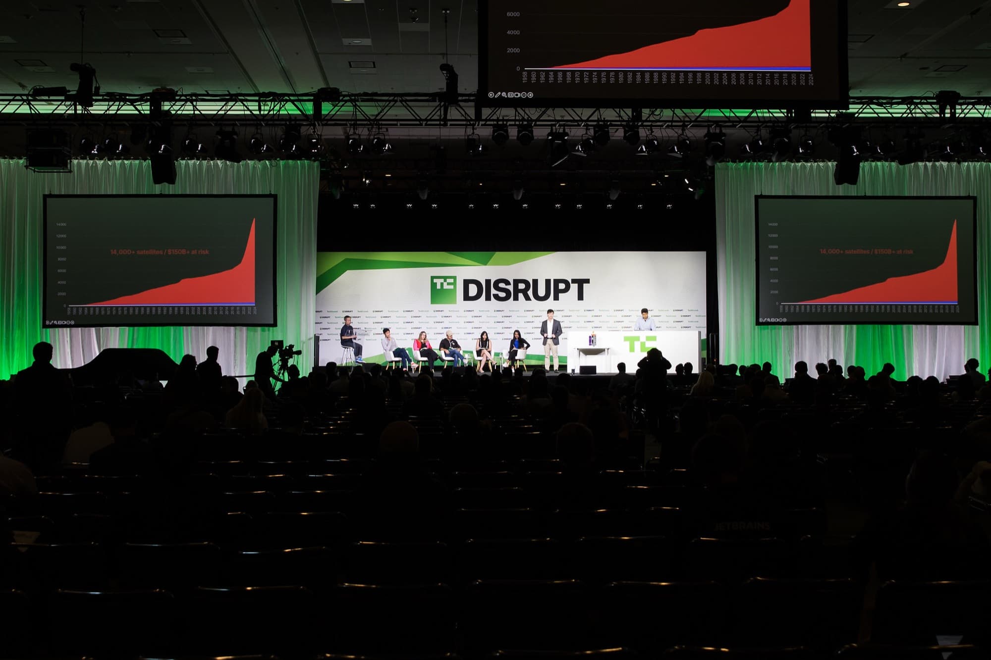 A packed TechCrunch Disrupt audience facing the green-lit main stage